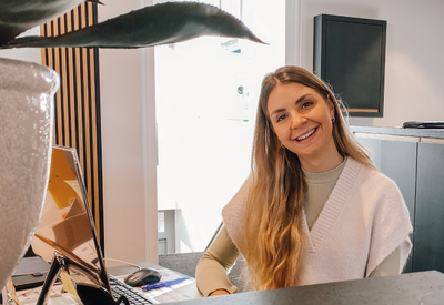 Mitarbeiterin Luisa Fersch sitzt an ihrem Schreibtisch im Büro des Autohaus Fersch und lächelt in die Kamera