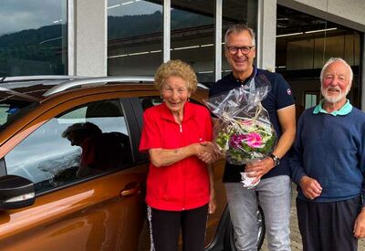 Thomas Fersch überreicht Blumenstrauß an älteres Ehepaar vor neuem Auto